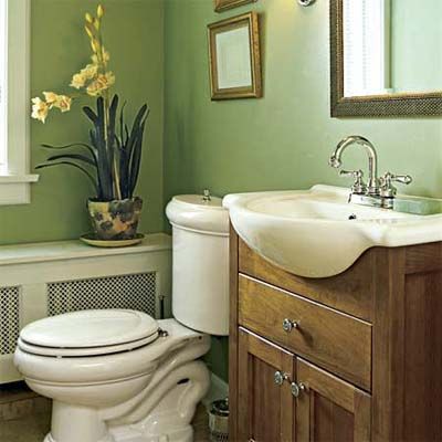 Half bathroom with green walls features a white toilet, a wooden vanity with a white sink, a plant in a decorative pot, and framed artwork on the walls.