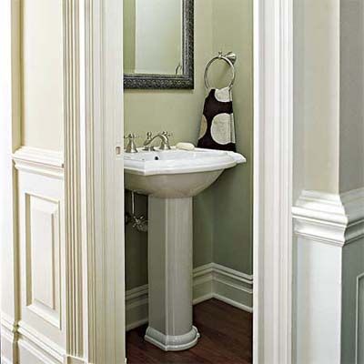 A compact half bath with a white pedestal sink, a dark-framed mirror and a towel ring.