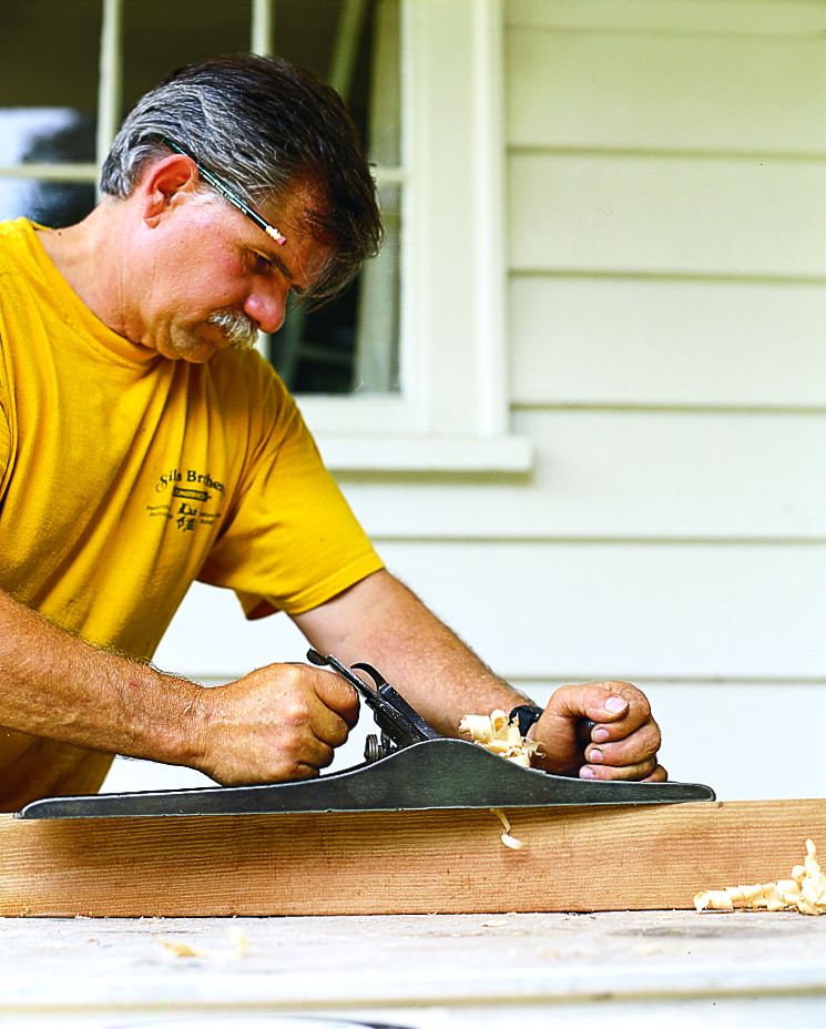 A man using a hand plane on a board of wood.