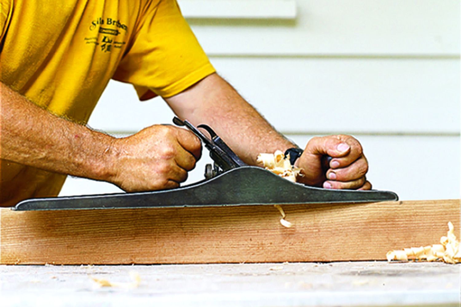 A man using a hand plane on a board of wood.