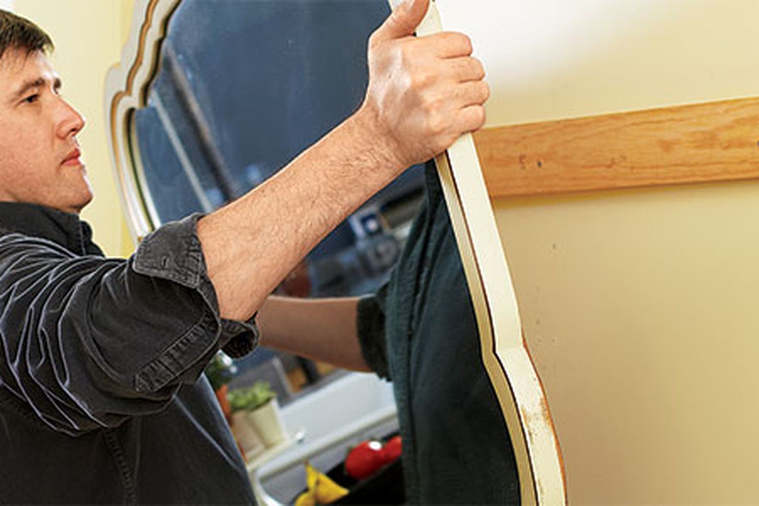 A person hangs a heavy mirror on the wall.