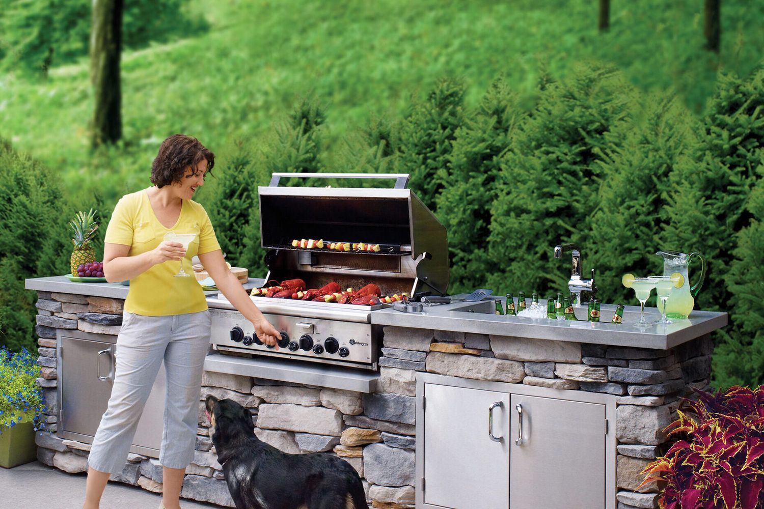 A woman standing in front of an outdoor kitchen with a grill and sink. A dog stands in front of her.