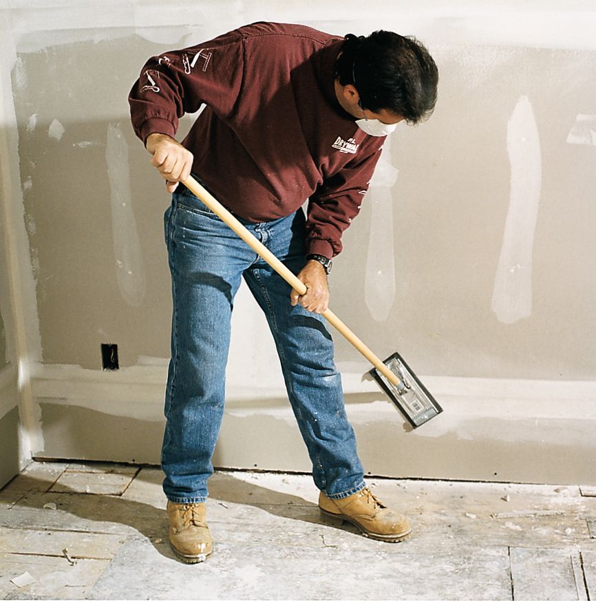 A man uses a swivel-head pole sander to sand as a step to finish drywall.