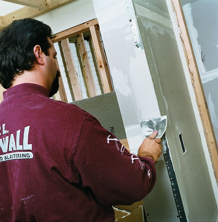 A man finishes drywall cornerbeads by using a drywall knife to cover the corner with a compound.