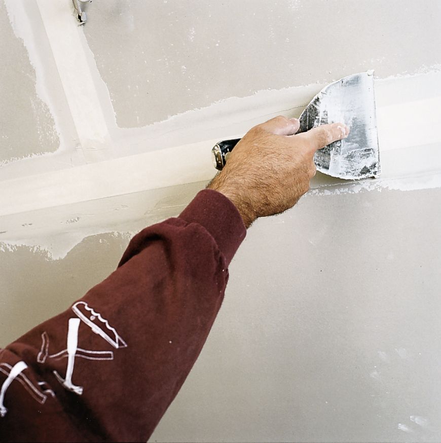 A man uses a drywall knife to cover the tape and finish drywall.