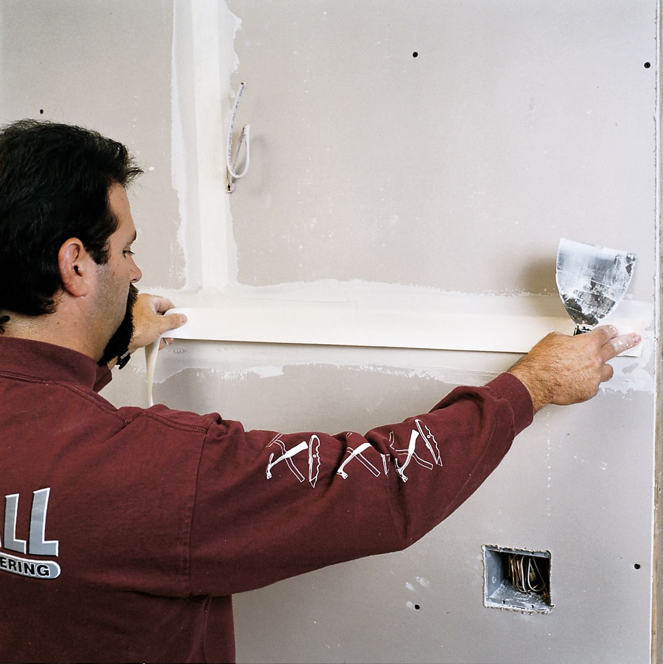 A man tapes a seam as he finishes drywall.