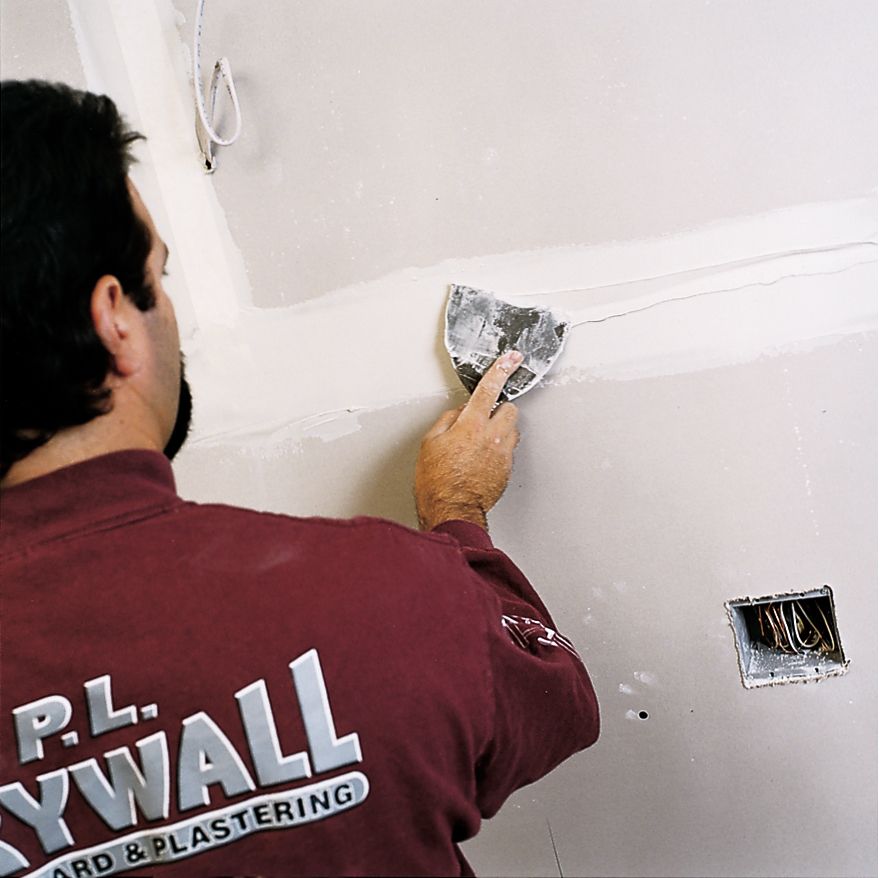 A man uses a drywall knife to finish drywall.