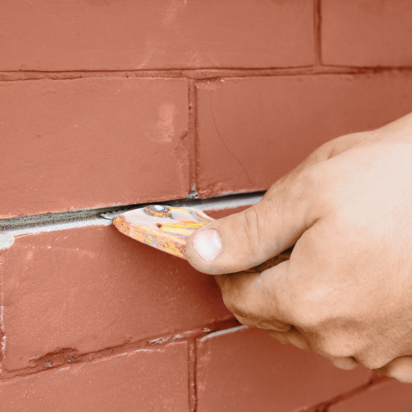 A person removing the old mortar from a brick wall.