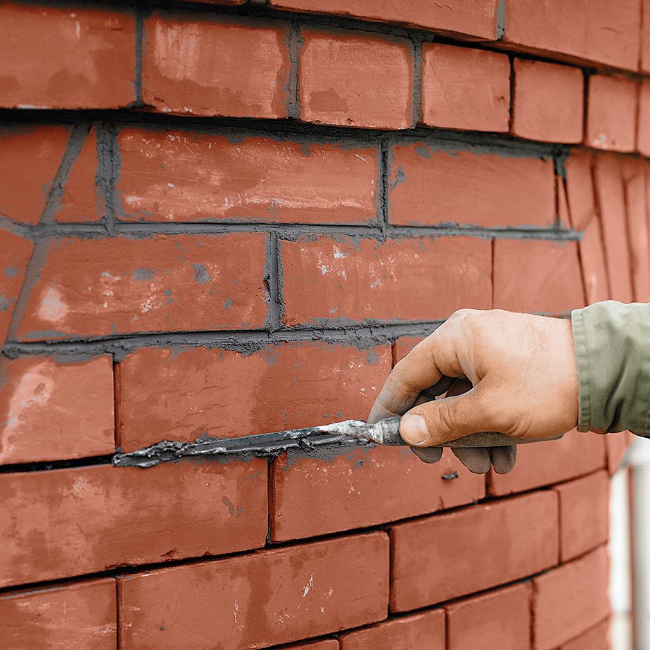 A person fills the brick wall joints with mortar.