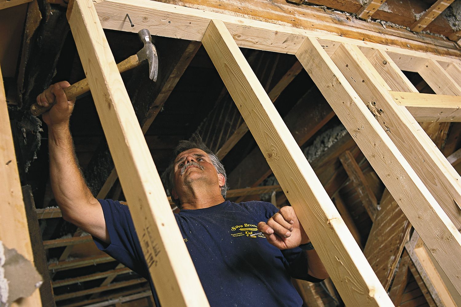 Builder hammers a partition wall frame into the ceiling to secure it in the room.
