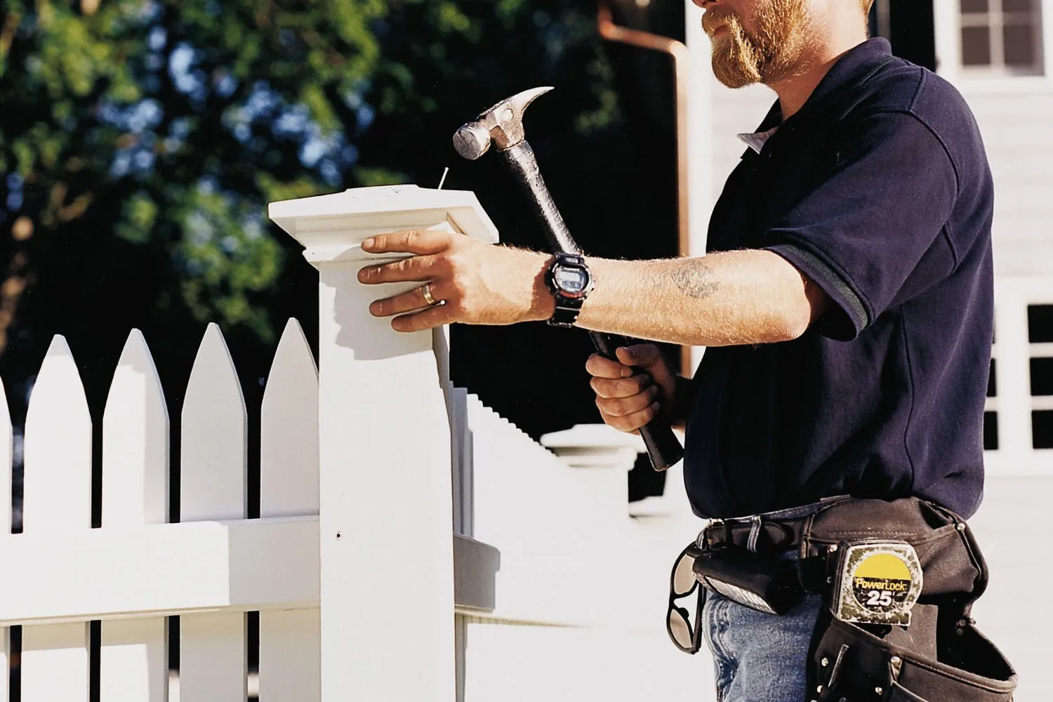 A man using a hammer to install the post of a picket fence.