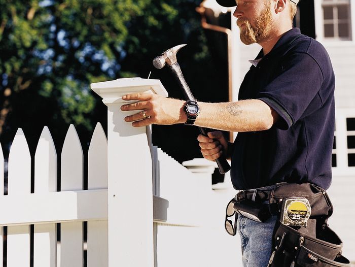 A man using a hammer to install the post of a picket fence.