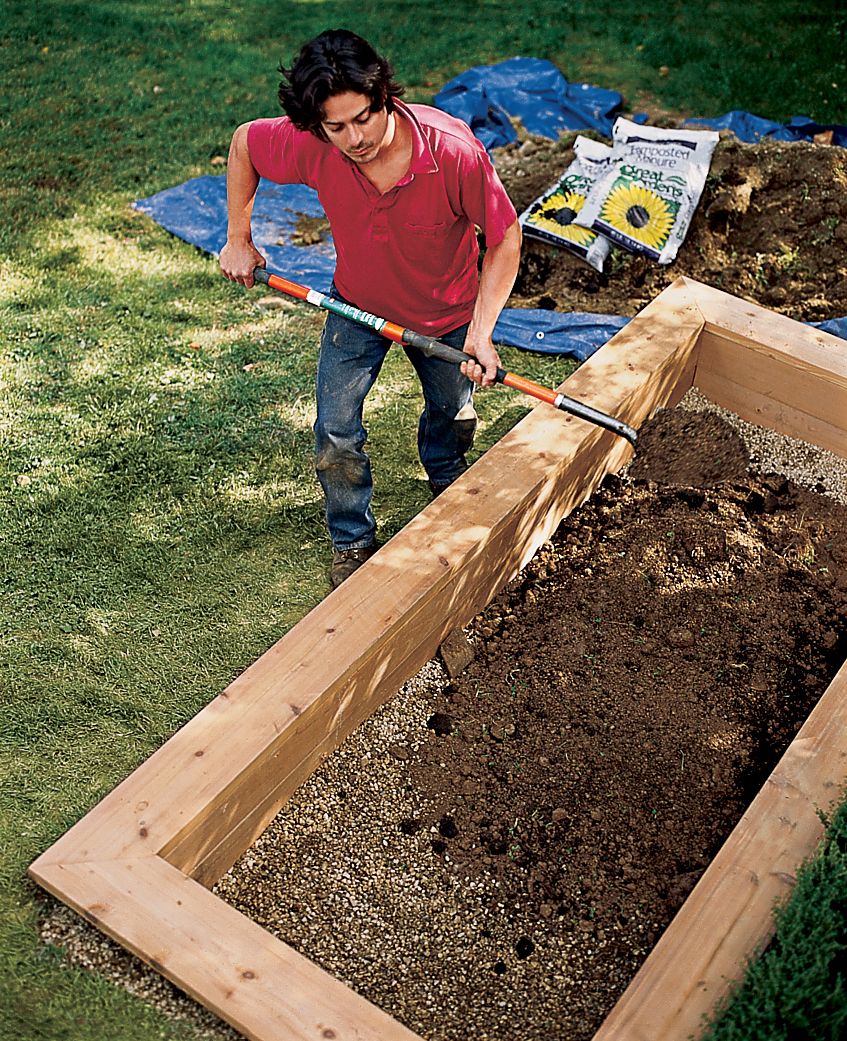 A man fills his raised planting bed.