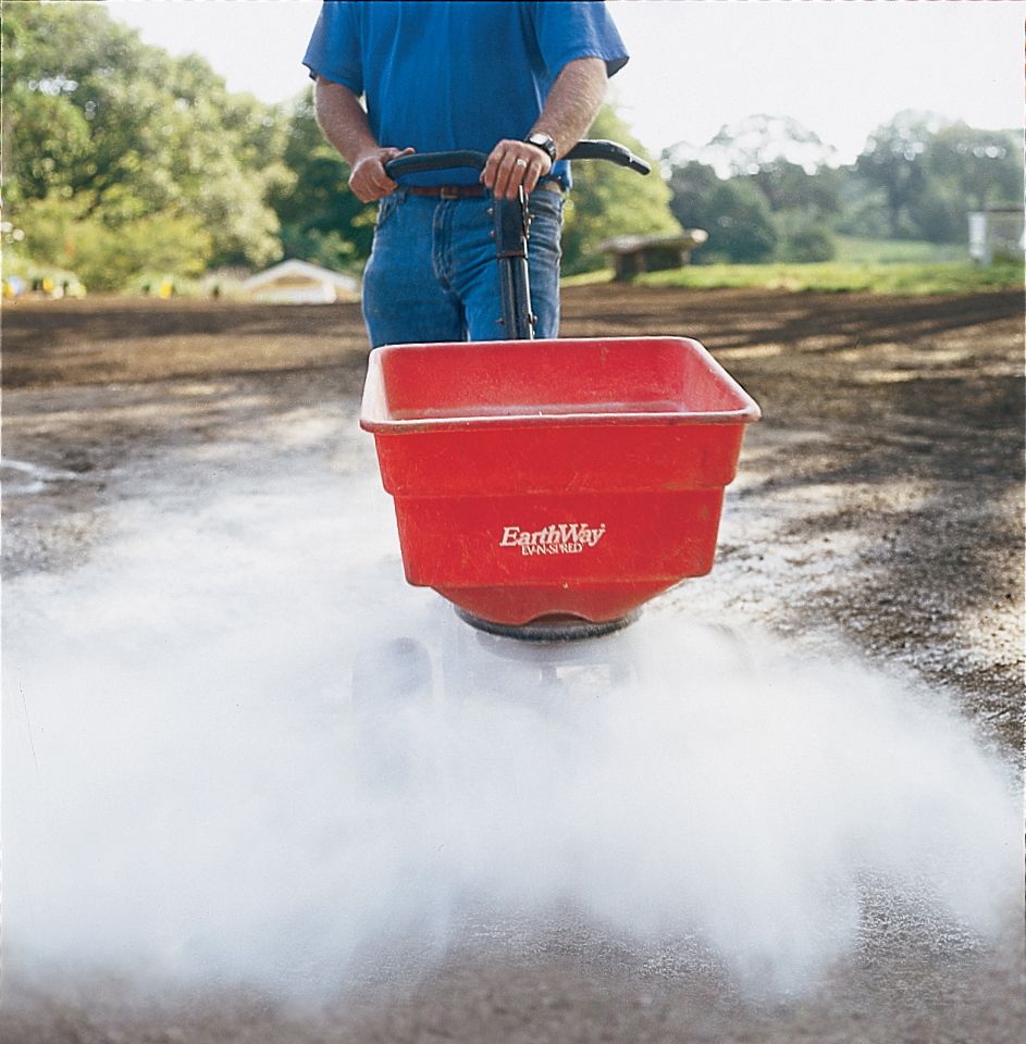 Man applying lime to the soil with a spreader.