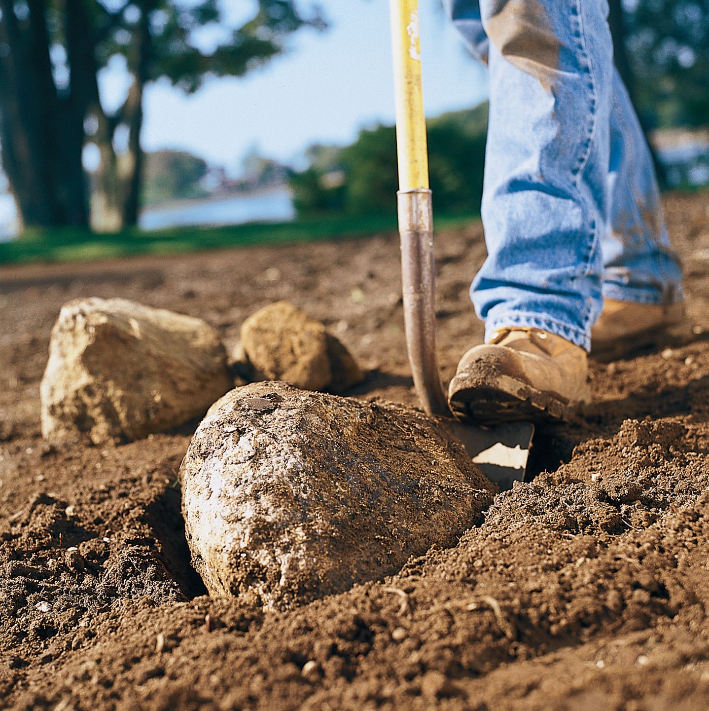 Man digging up old soil and rocks with shovel.