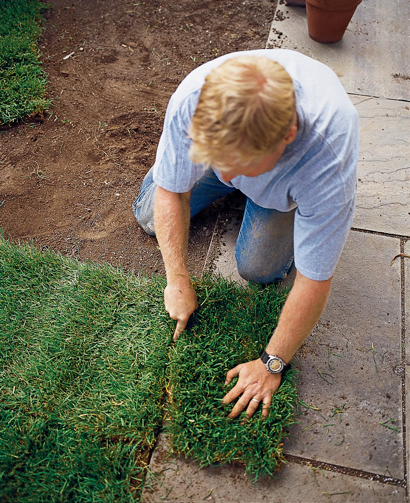 A landscaper cuts off extra sod where it meets the sidewalk.