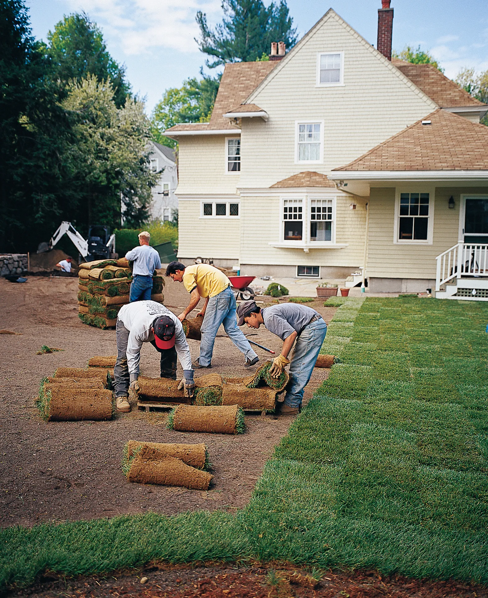A team of landscapers lay subsequent rows of sod to create a new lawn.
