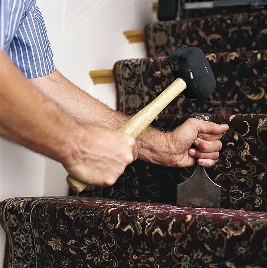 A person uses a rubber mallet and a carpet tool to pack the stair runner into the steps.