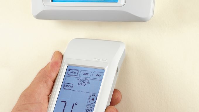 Photo of a person adjusting their programmable thermostat with a remote.