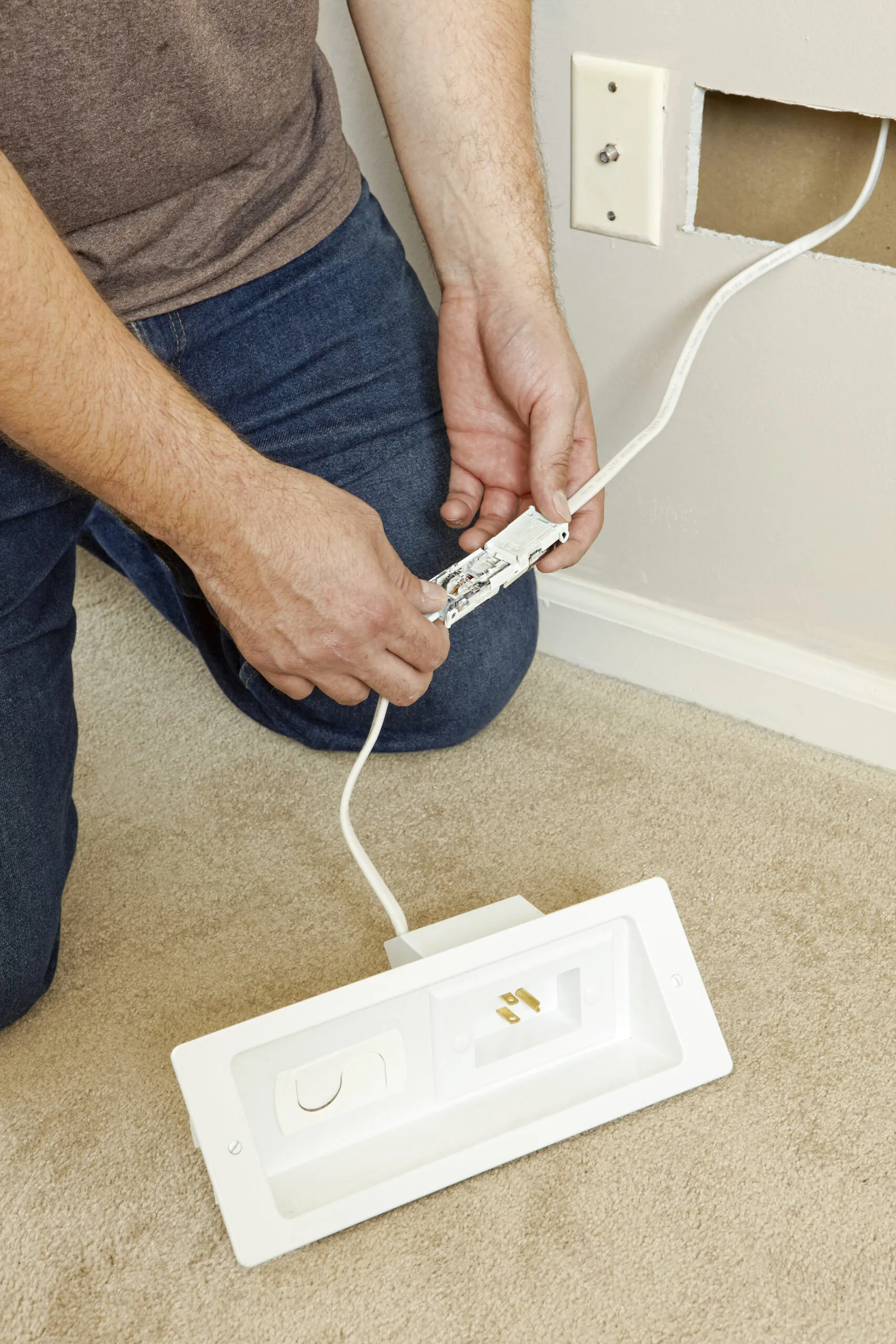 A person connecting an electrical wire to a power outlet component, preparing to install it in a wall opening as a step in mounting a TV.