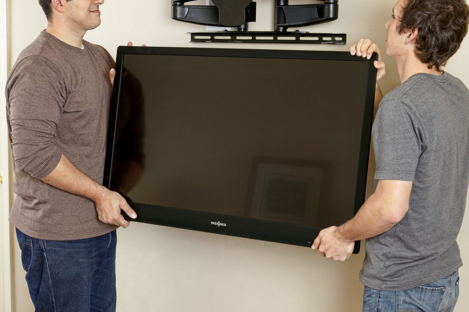 Two men lift ang hang a flat-screen TV on a TV wall mount.