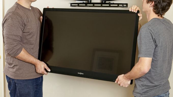 Two men lift ang hang a flat-screen TV on a TV wall mount.