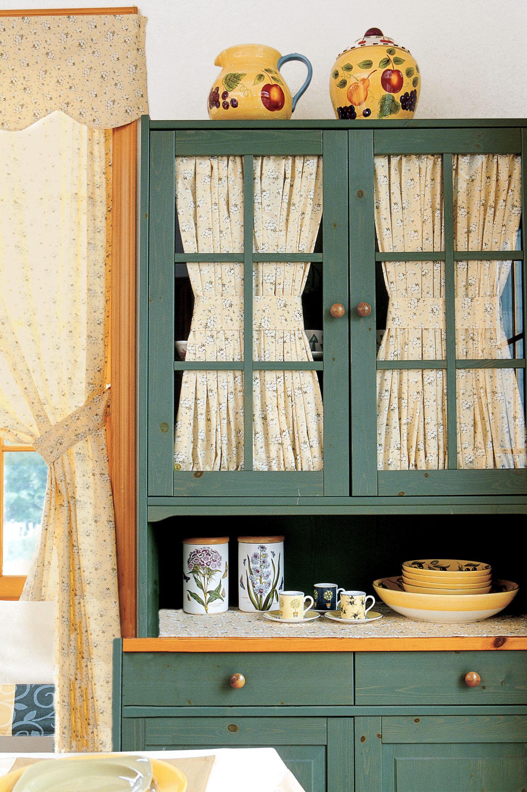 A set of green cabinets in a kitchen with pitchers on top of them.