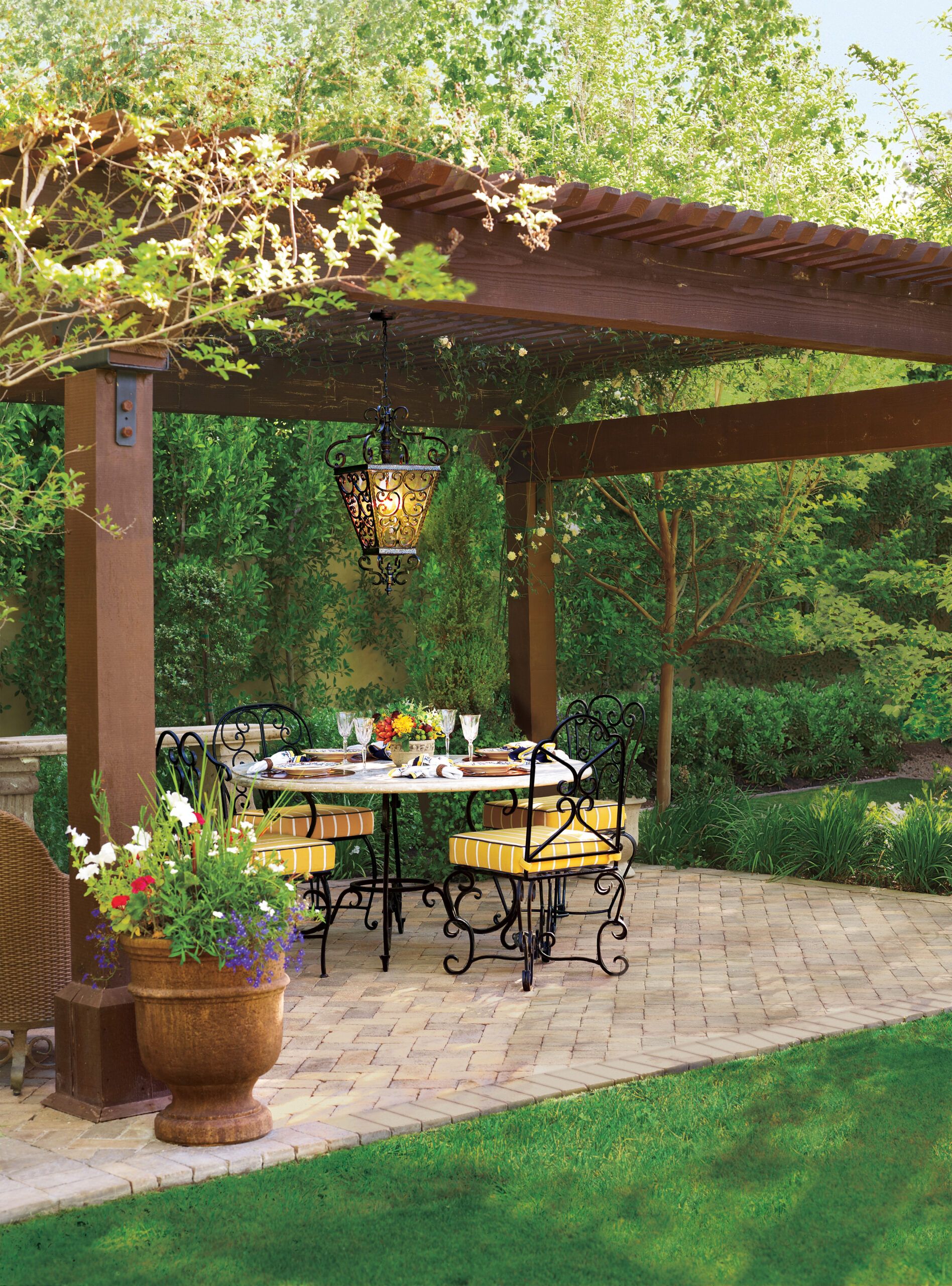 An outdoor patio, with a round table and seats below a wooden roof.