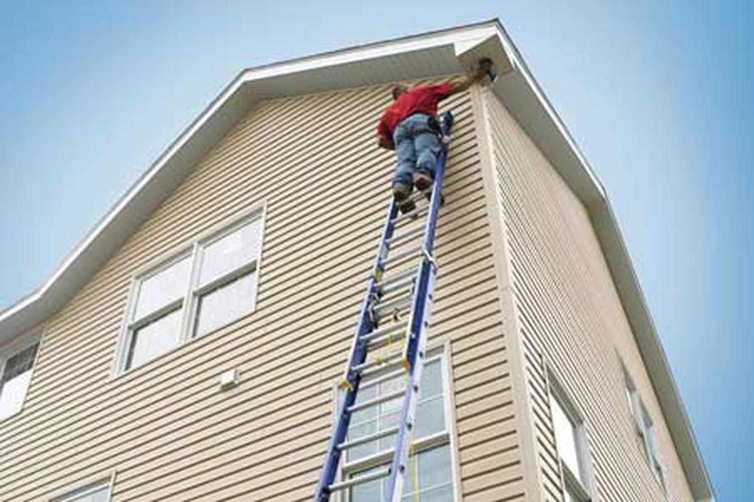 A man standing on a blue ladder working on the side of a house.