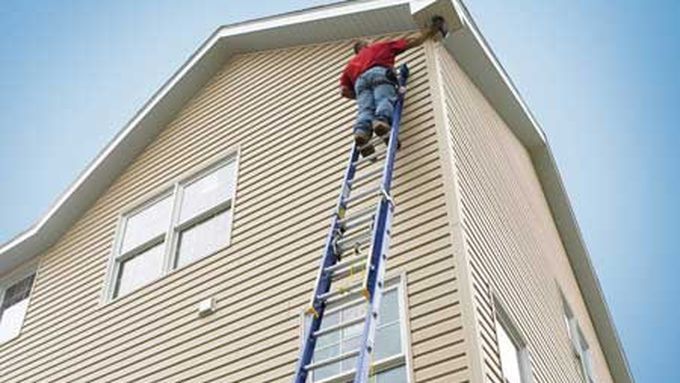 A man standing on a blue ladder working on the side of a house.