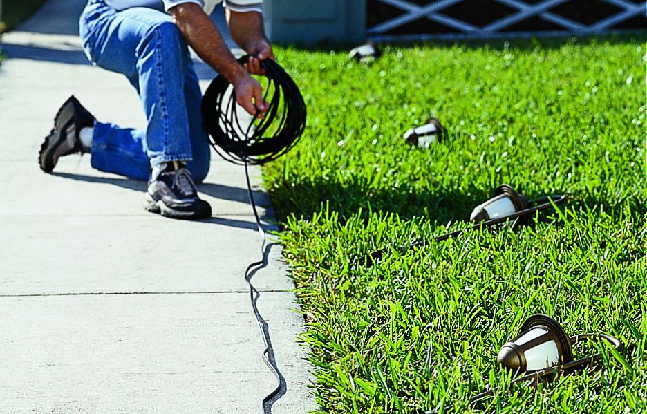 A man lays out landscaping lights and wire.