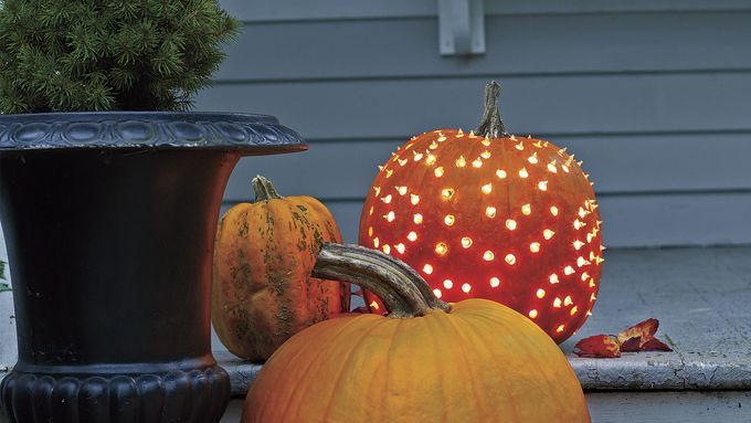 A beautiful pumpkin luminary sits on a front step along with other pumpkins.