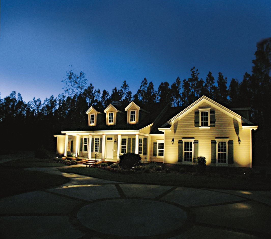 A yellow house at night lit by landscape lights shining against it's front.