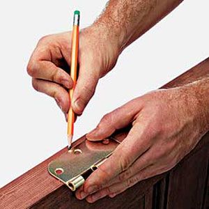 using a pencil and hinge to mark the place on the door where the mortise needs to be cut