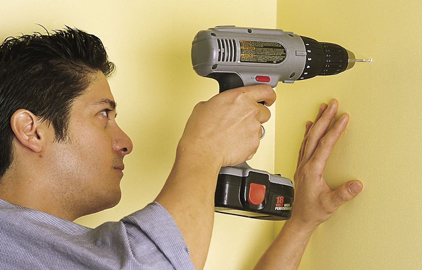 A person drills a pilot hole into a walk in preparation for hanging wall-mounted shelves.