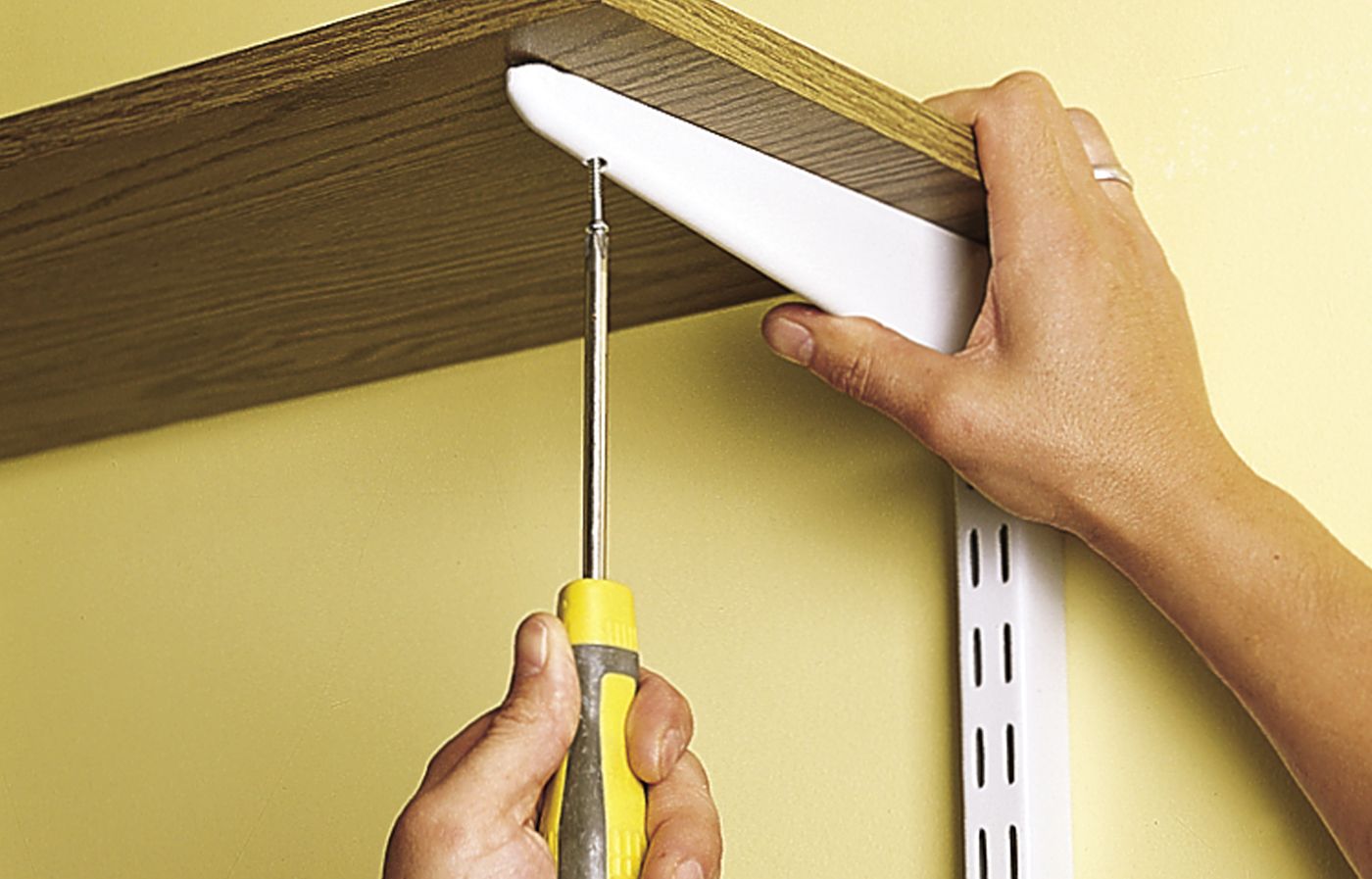 A person screws shelves into shelf standards to mount them to the wall.