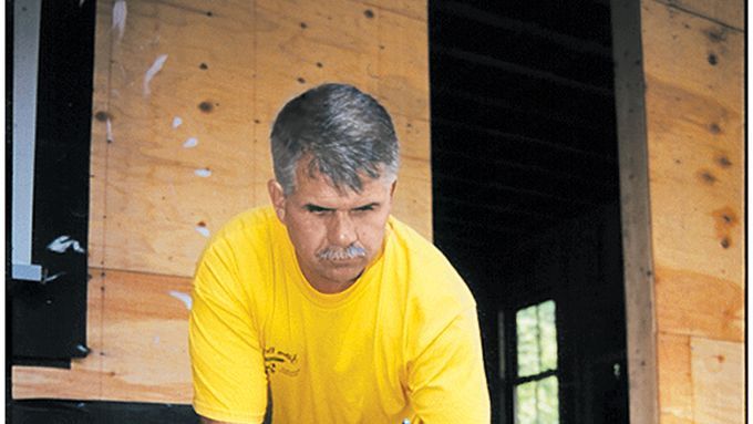 A man inspecting a deck and applying an adhesive to it.