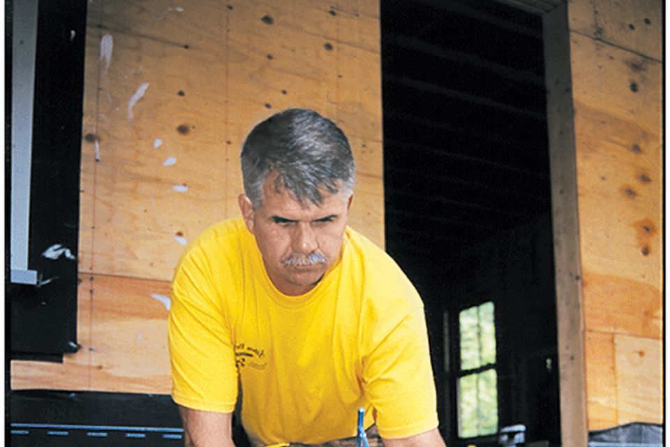 A man inspecting a deck and applying an adhesive to it.