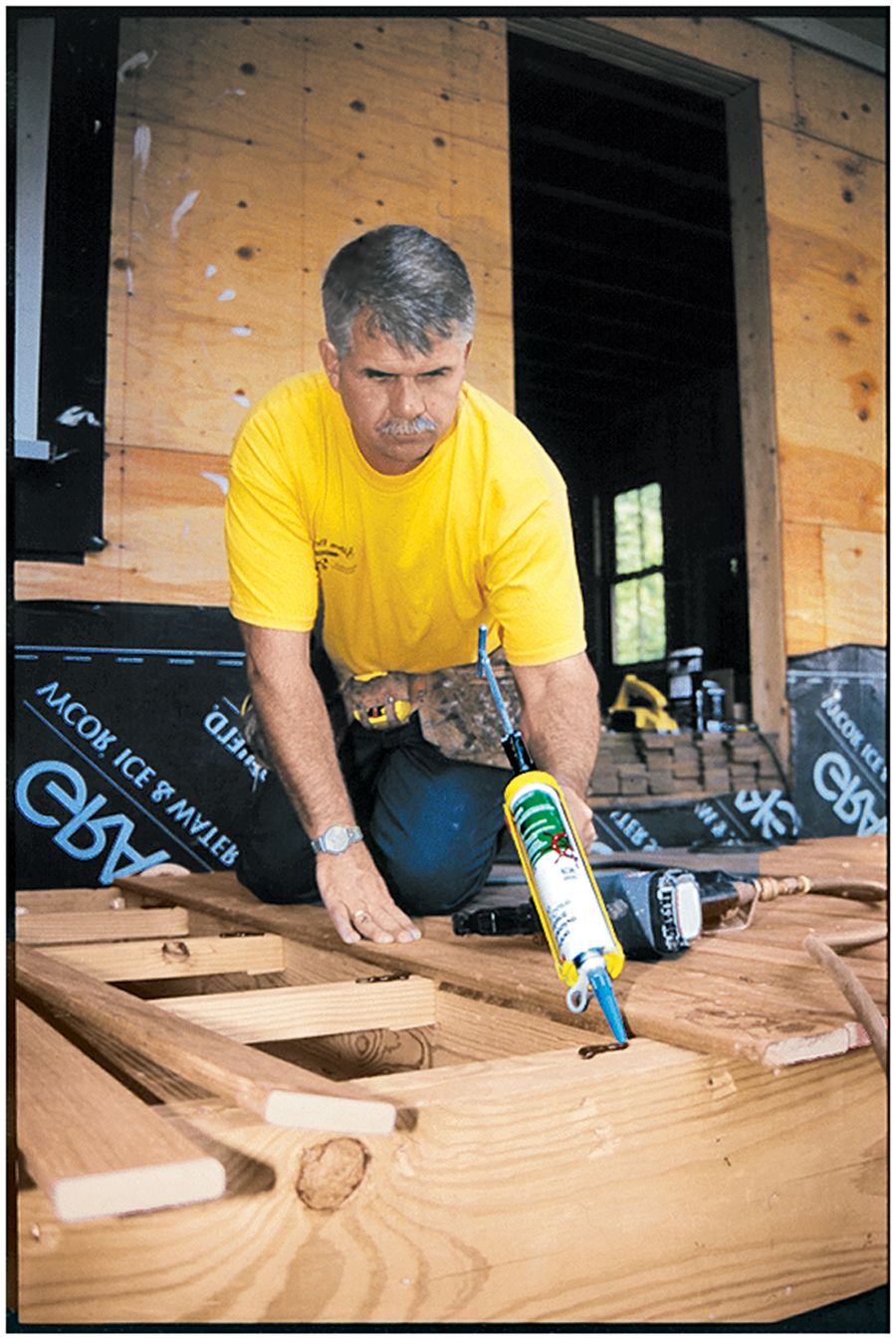 A man inspecting a deck and applying an adhesive to it.