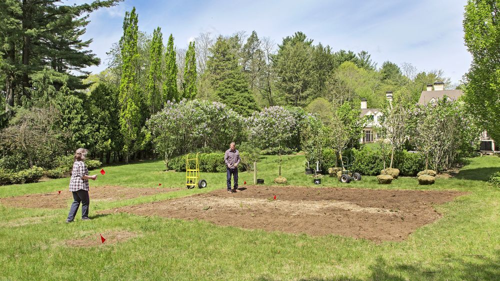 A dirt area is marked off for planting an orchard and trees sit nearby waiting to be planted.