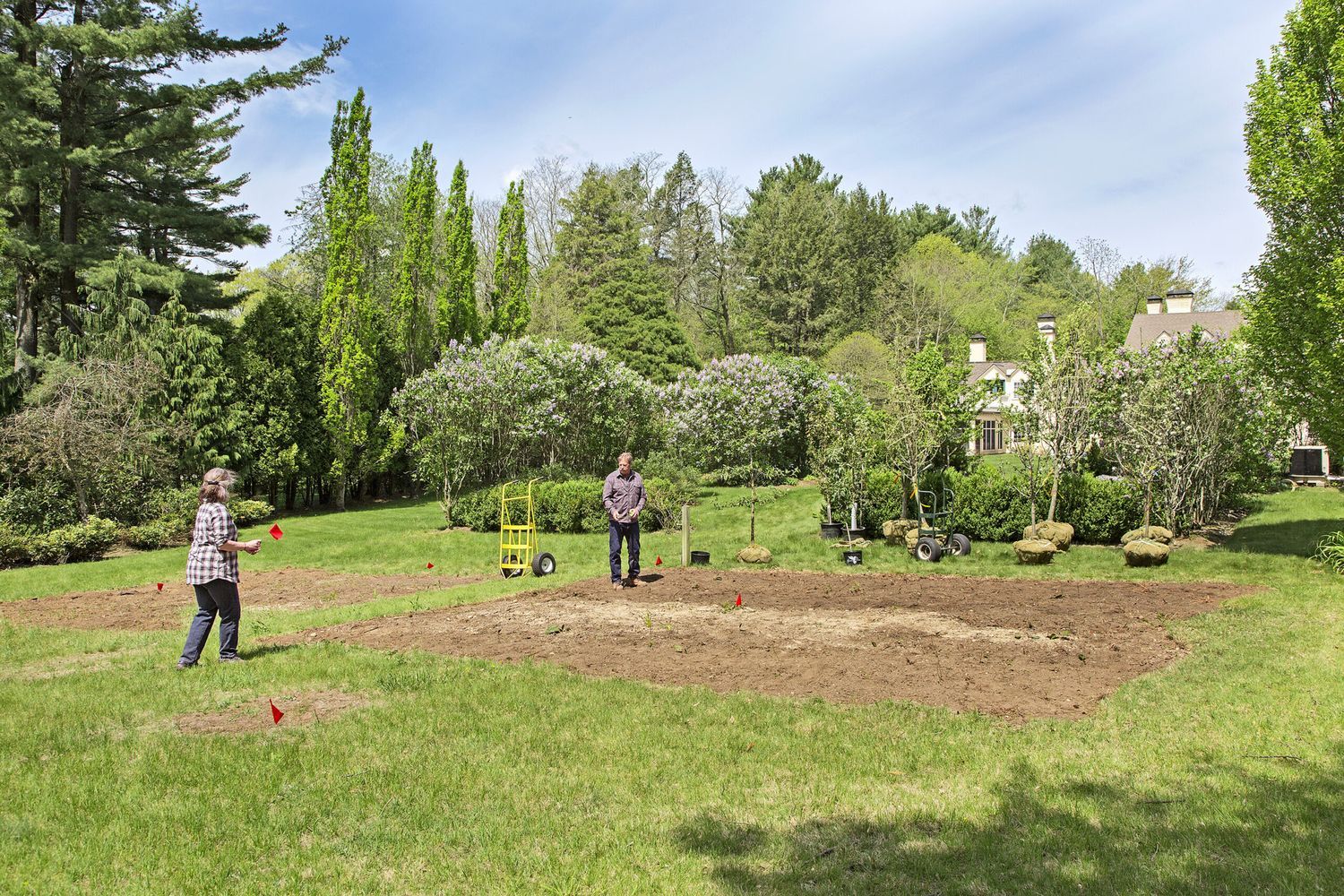 A dirt area is marked off for planting an orchard and trees sit nearby waiting to be planted.