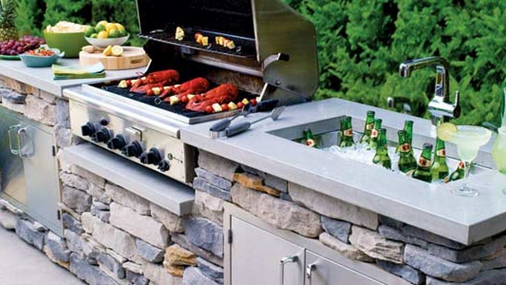 Outdoor kitchen with a grill, sink, and fridge.