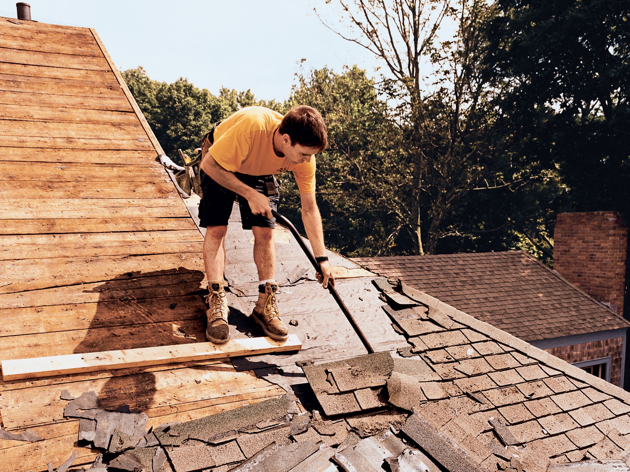 Silva Brothers crew member Garrett DeBlois takes a prybar to 22-year-old asphalt roof shingles at the Manchester-By-the-Sea project house, which had begun to leak.