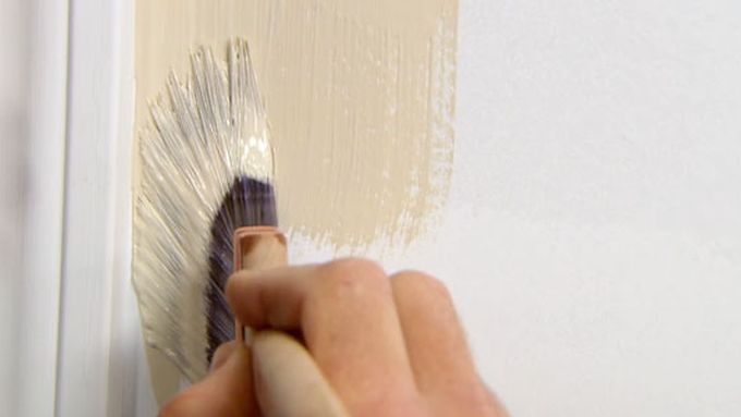 A paint brush being used to paint the edge of a wall and a piece of crown molding.