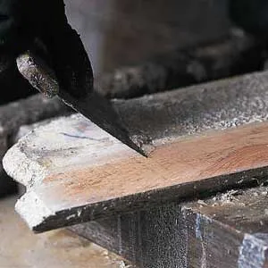 A putty knife being used to scoop the finish off of a piece of wood.