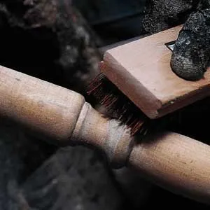 A bristle scrub brush being used to remove caked-in paint from a table leg.