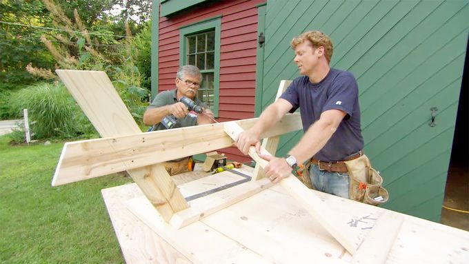 Two men constructing a picnic table in a yard.