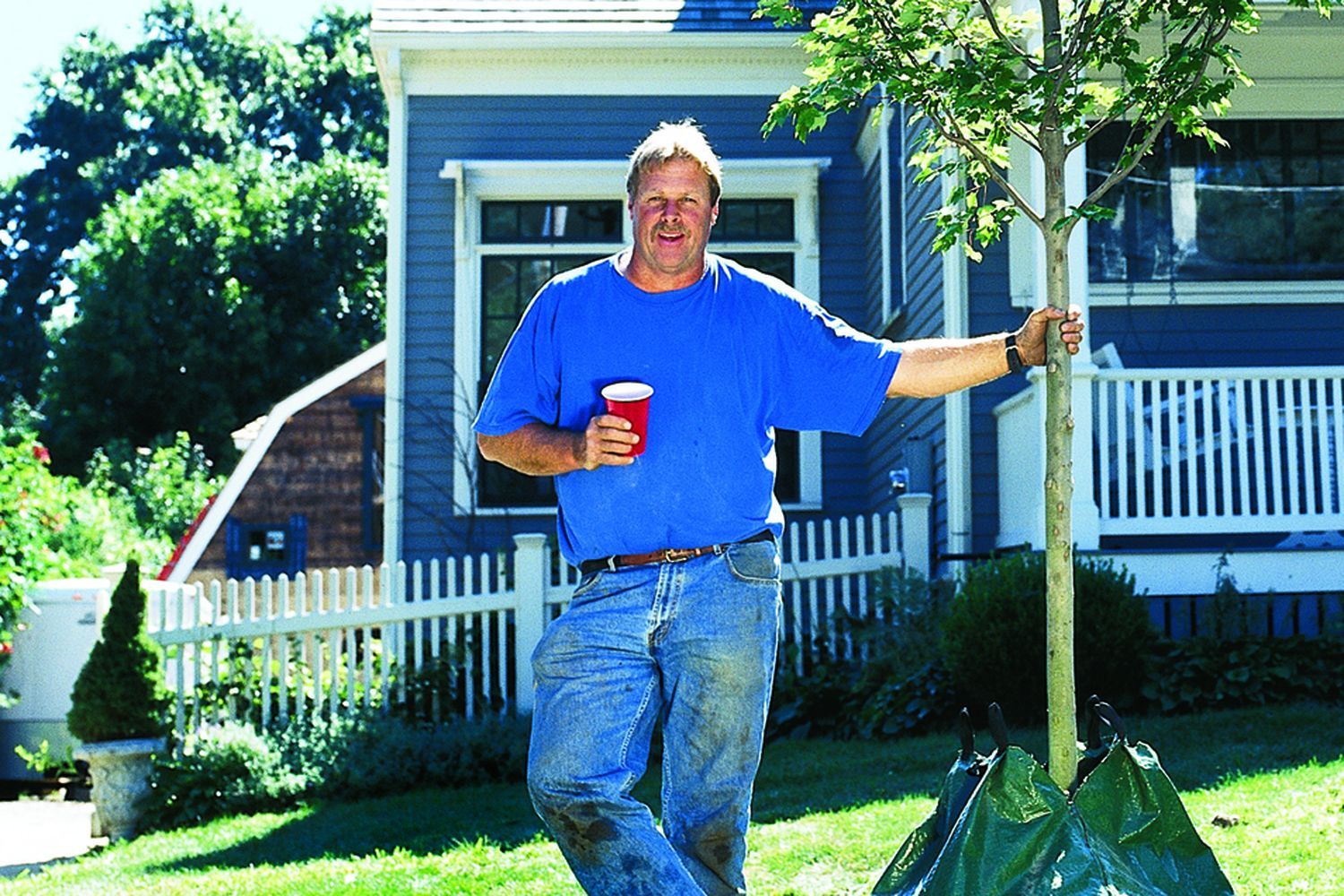 A man standing by a tree he recently planted.