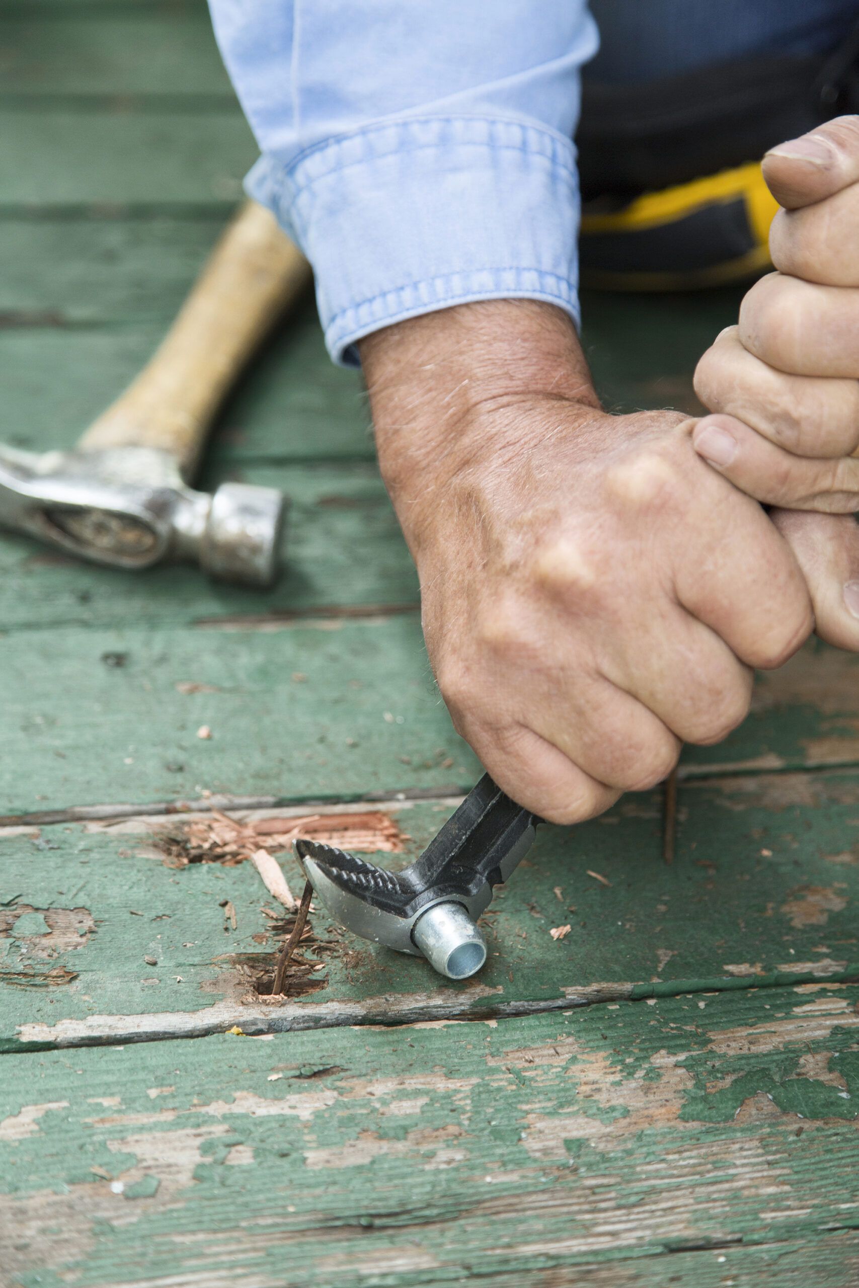 using a hammer to pull the nails out of a porch board