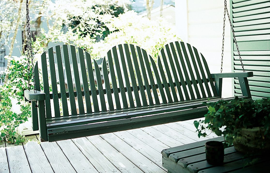 A green porch swing hanging over a wooden porch.